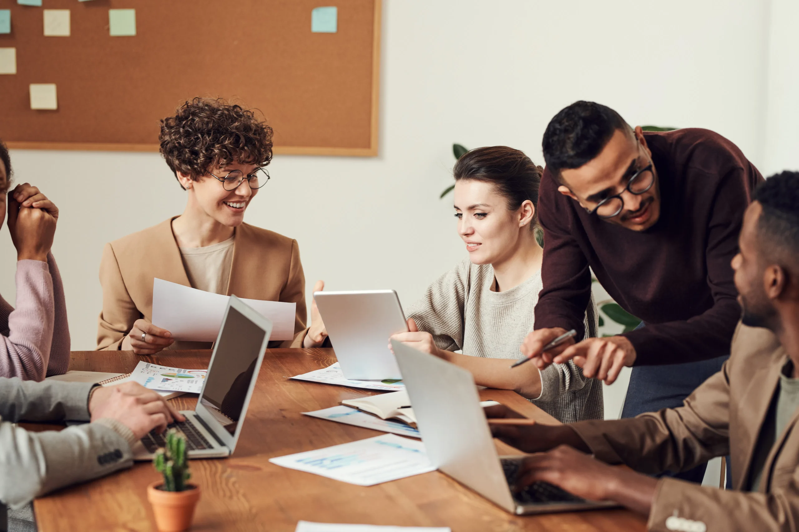 A diverse group of professionals collaborate around a table with laptops and tablets, discussing ESG reporting course strategies and sustainable investing course options.
