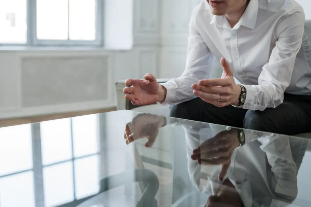 A person in a white shirt sits at a glass table, gesturing with their hands, possibly during an ESG consulting session to discuss sustainable business strategies.