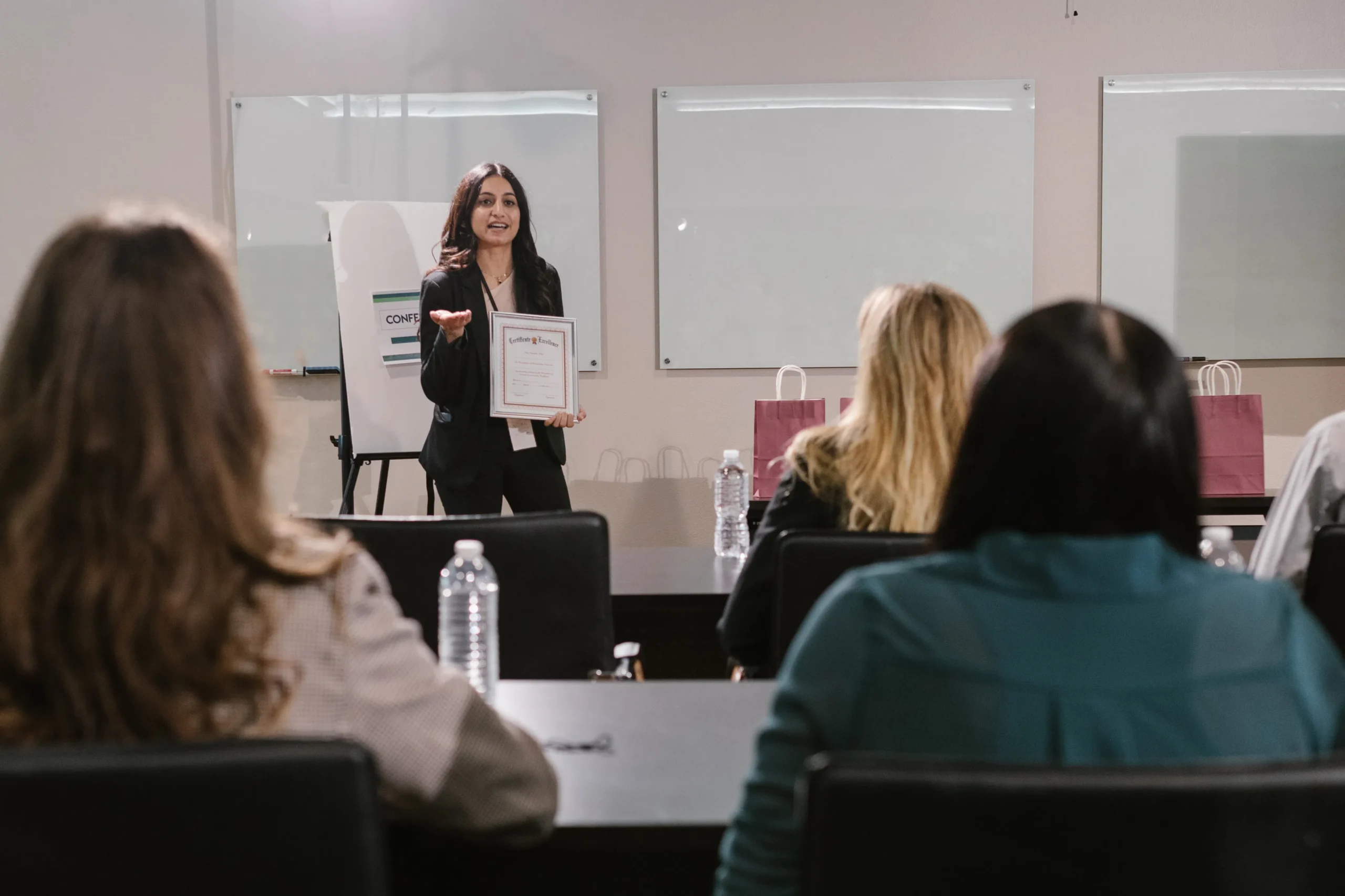 A woman giving a presentation, possibly about ESG training certification, holding a certificate in front of an audience, highlighting the importance of ESG courses and ESG reporting training for professionals.
