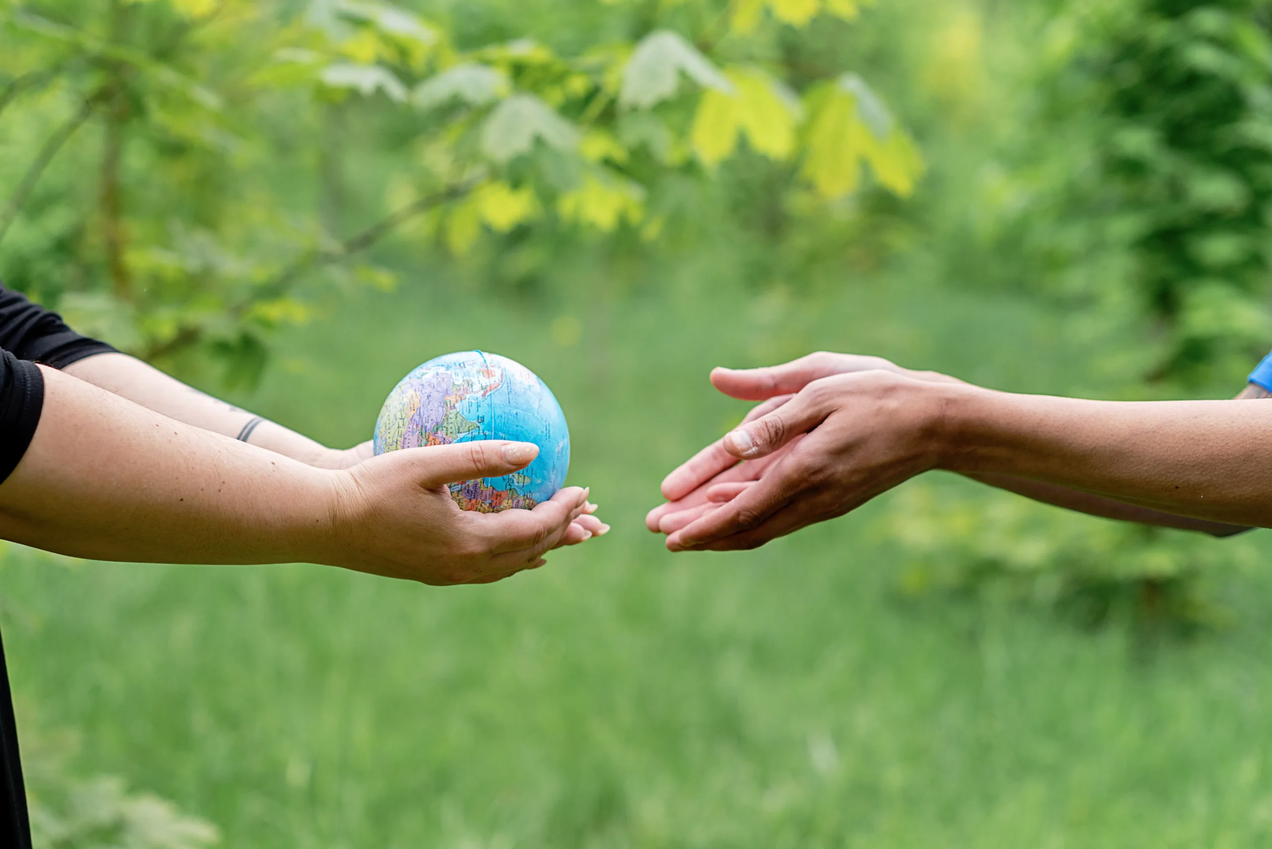 A small globe being passed between two people, representing the global impact of ESG and the opportunities available through ESG courses and ESG training programs.