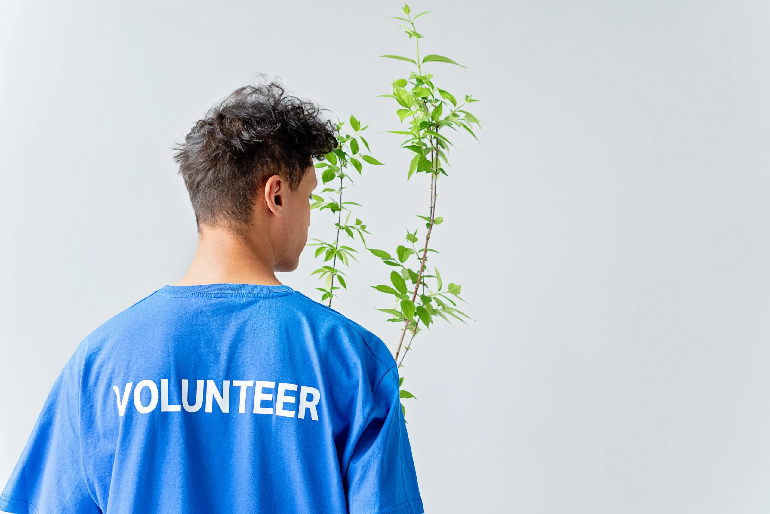 A volunteer wearing a blue shirt looks at a small tree, representing the environmental and social responsibility aspects of ESG and the benefits of ESG investing courses.