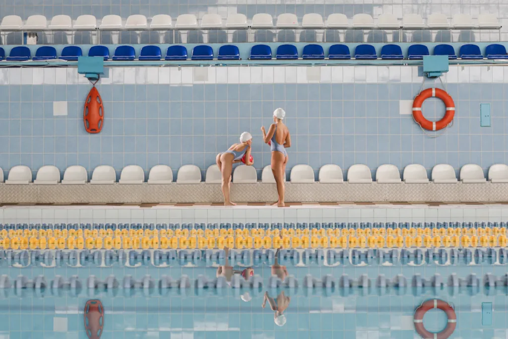 Two female swimmers in swimsuits and caps stand near a pool with multiple lanes, which could represent the need for robust ESG training and online ESG courses to ensure businesses stay afloat and navigate complex environmental, social, and governance challenges.